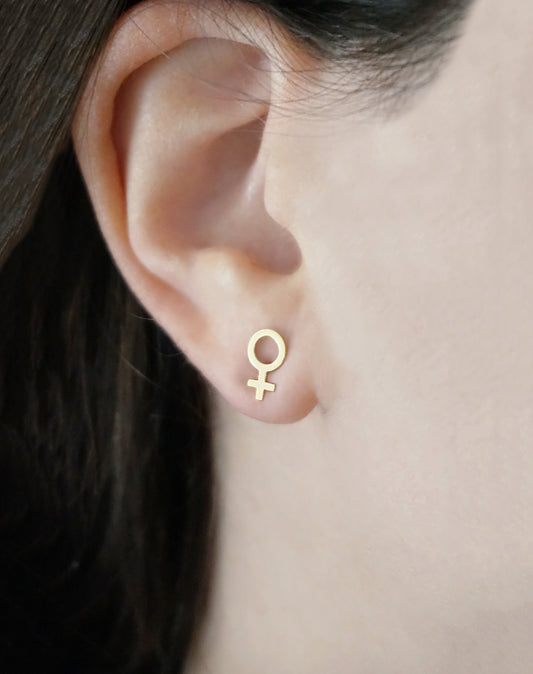 female wearing small solid yellow gold female/Venus symbol stud earrings