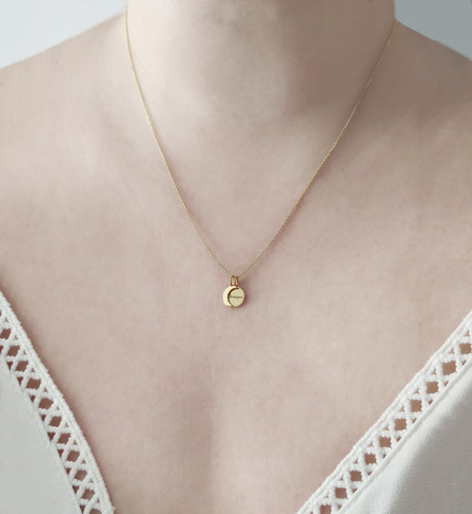 woman wearing gold necklace with two small charms, a crescent moon and a personalized disc
