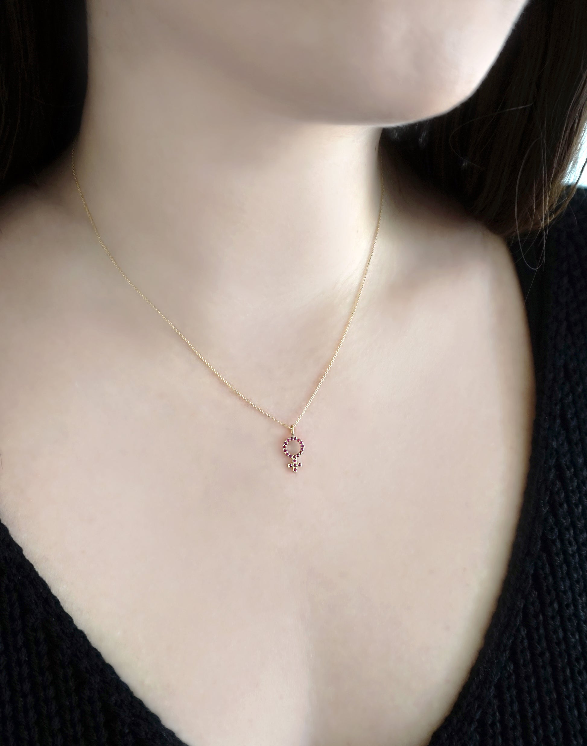 woman wearing a gold necklace with a small venus female symbol pendant set with Rubies