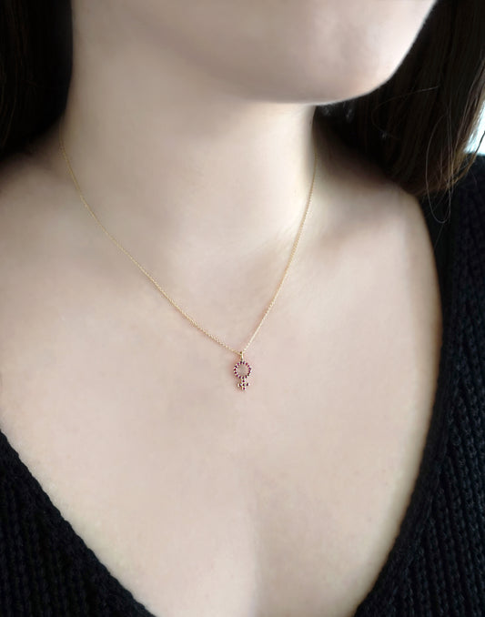 woman wearing a gold necklace with a small venus female symbol pendant set with Rubies