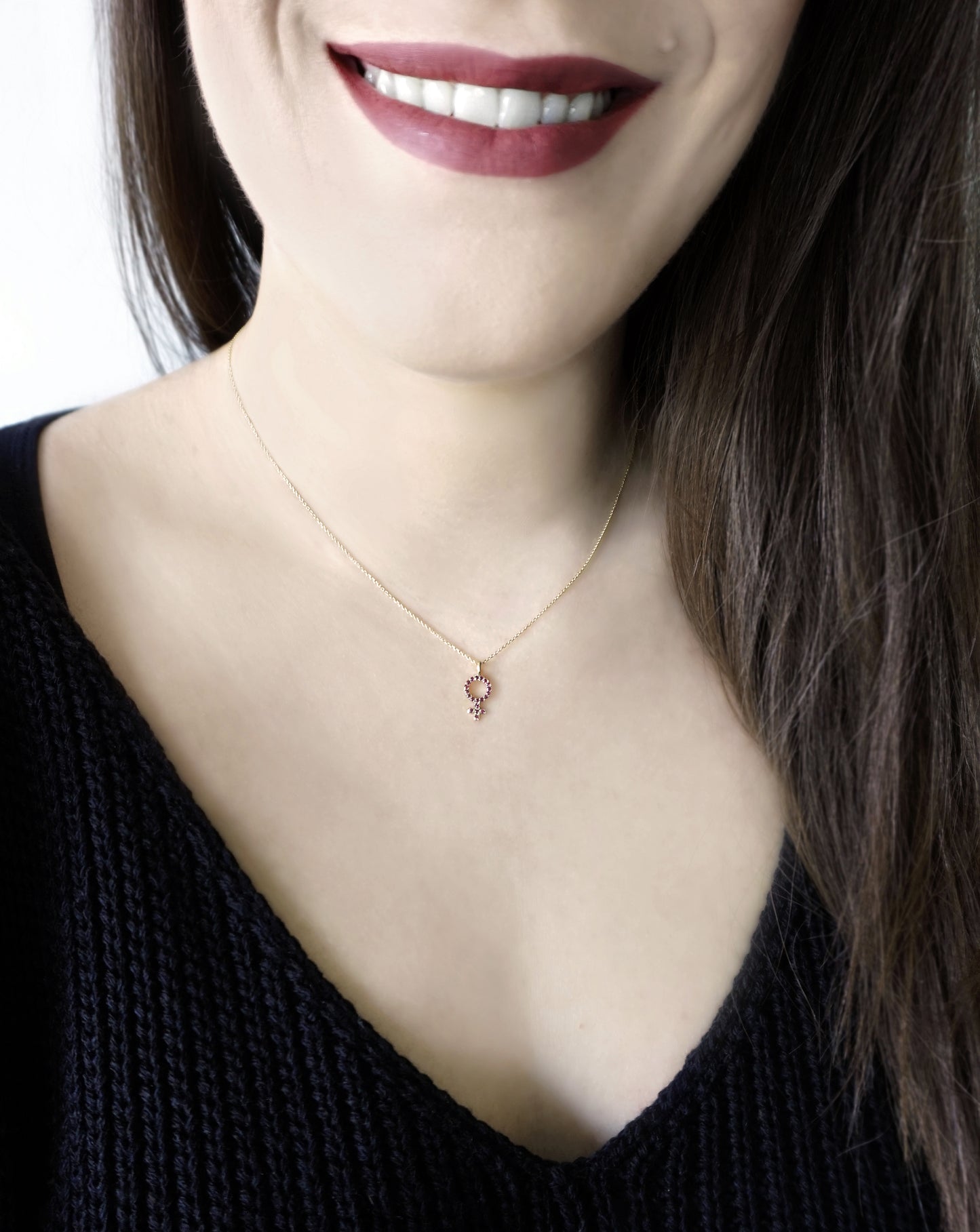 woman wearing a delicate gold necklace with a small venus female symbol pendant set with Rubies