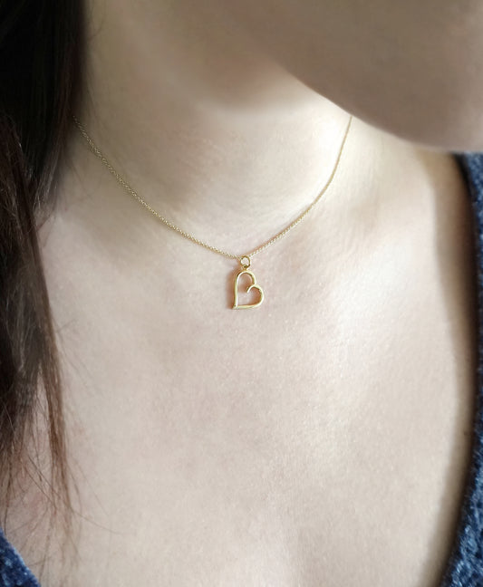 close up of a woman's neck wearing a gold necklace with a small sideways heart pendant