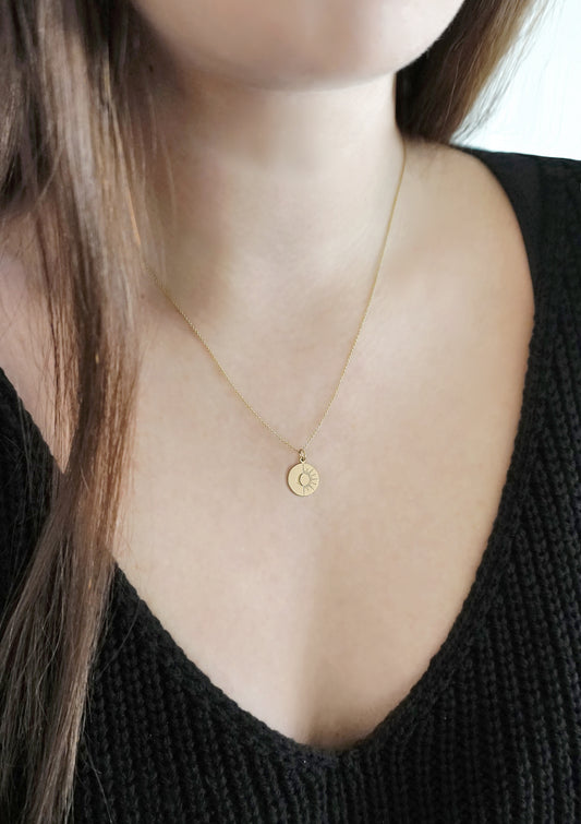 female wearing solid gold disc pendant necklace engraved with a sun and moon design