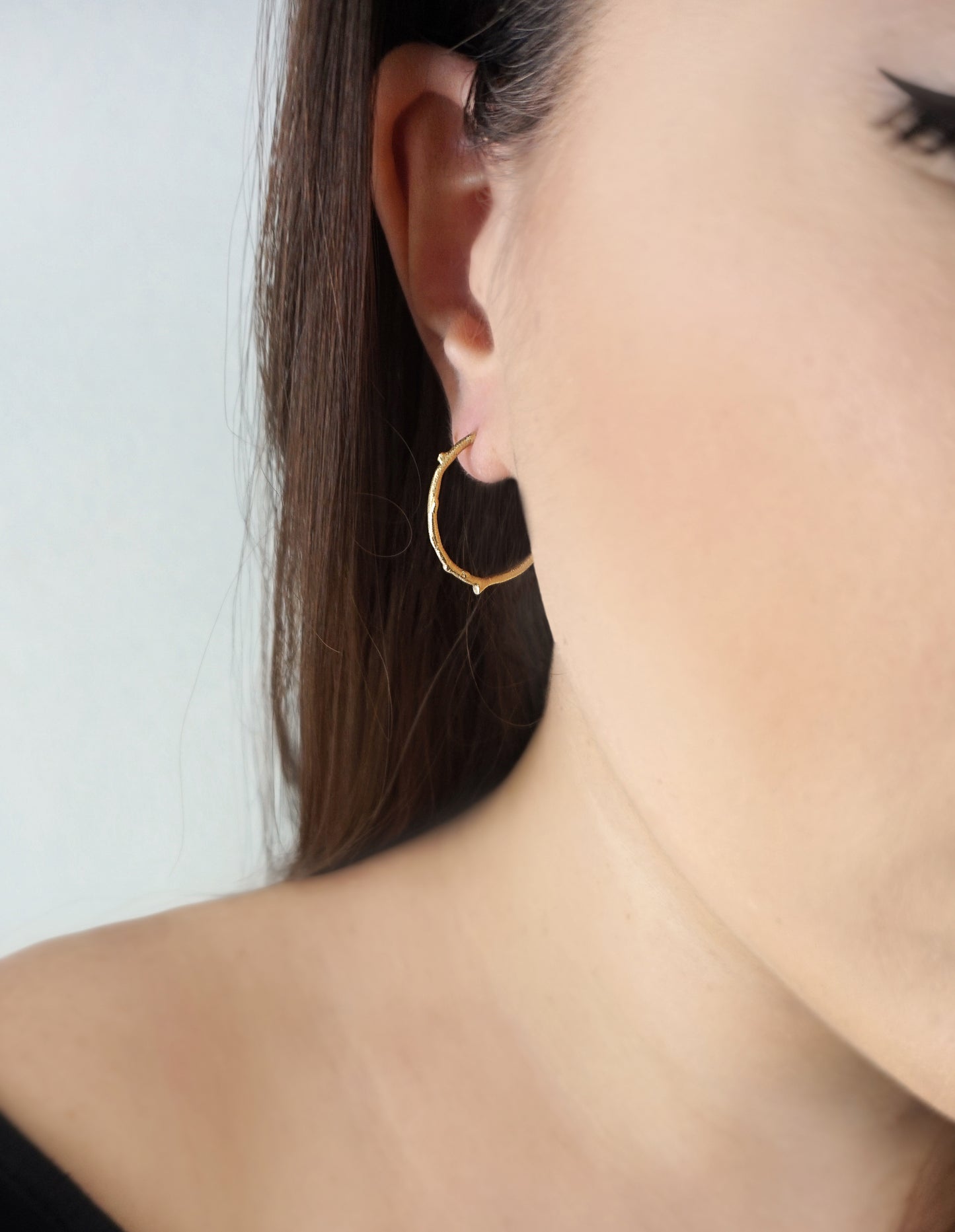 close up of a woamn wearing gold hoop earring with a twig branch like design with brushed polished finish