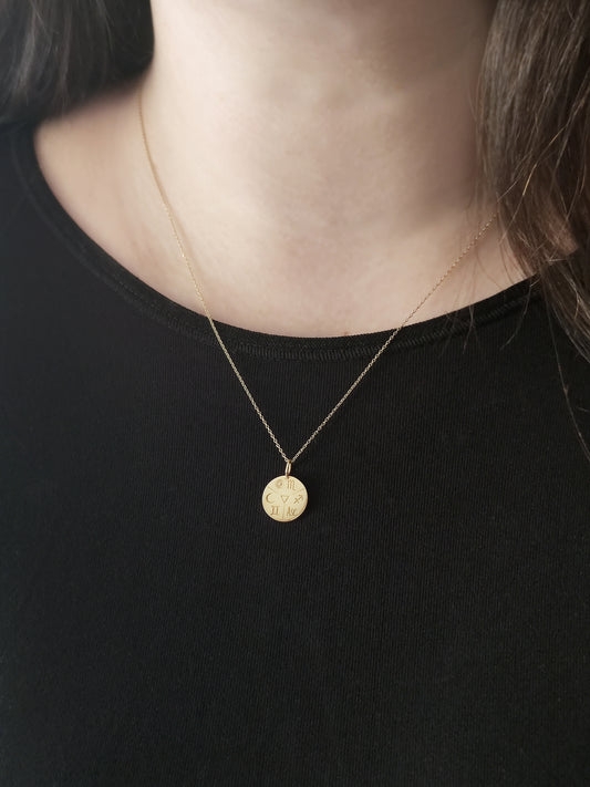 woman wearing gold disc pendant necklace personalized with natal chart zodiac signs of the sun the moon and ascendant and an alchemy element in the center