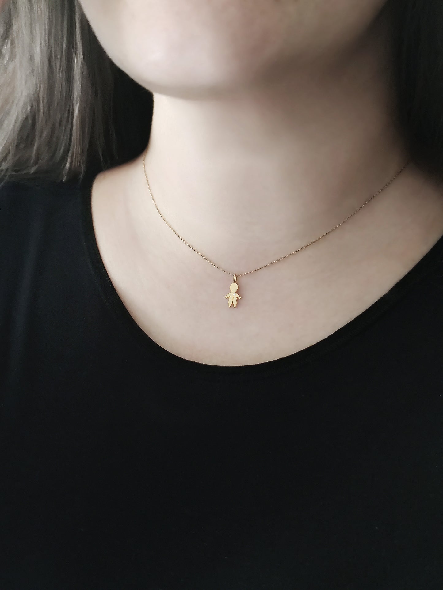 close up of a woman's neck wearing a gold necklace with a tiny boy charm engraved with a monogram and set with a tiny diamond