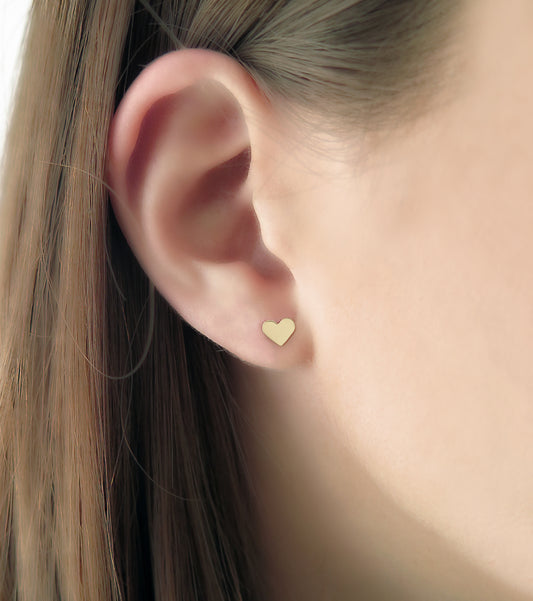 woman wearing tiny solid gold heart-shaped stud earrings with polished finish