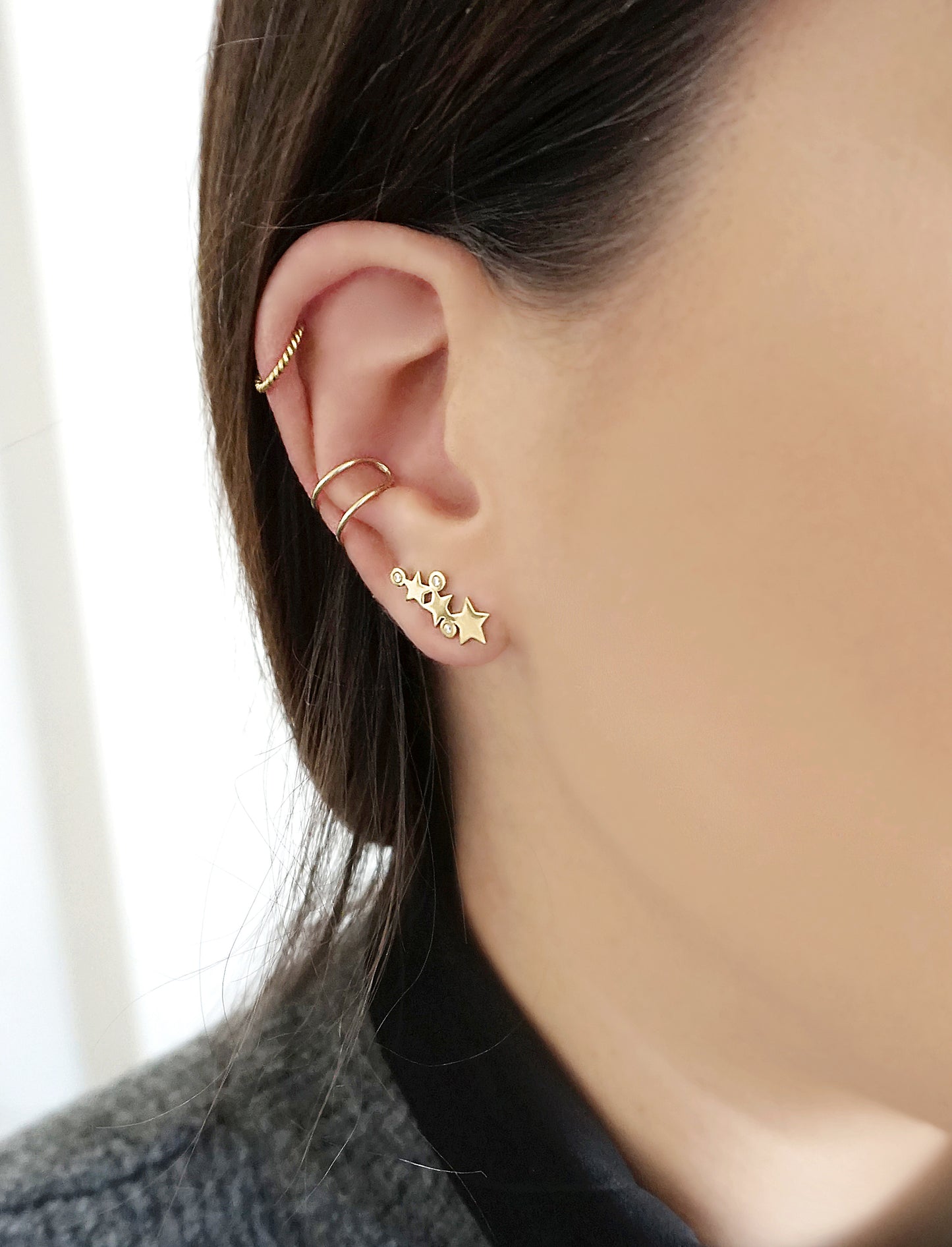 woman wearing 14K yellow gold triple star climber earrings with three tiny diamonds, a twisted no piercing hoop and a double bar no piercing open hoop