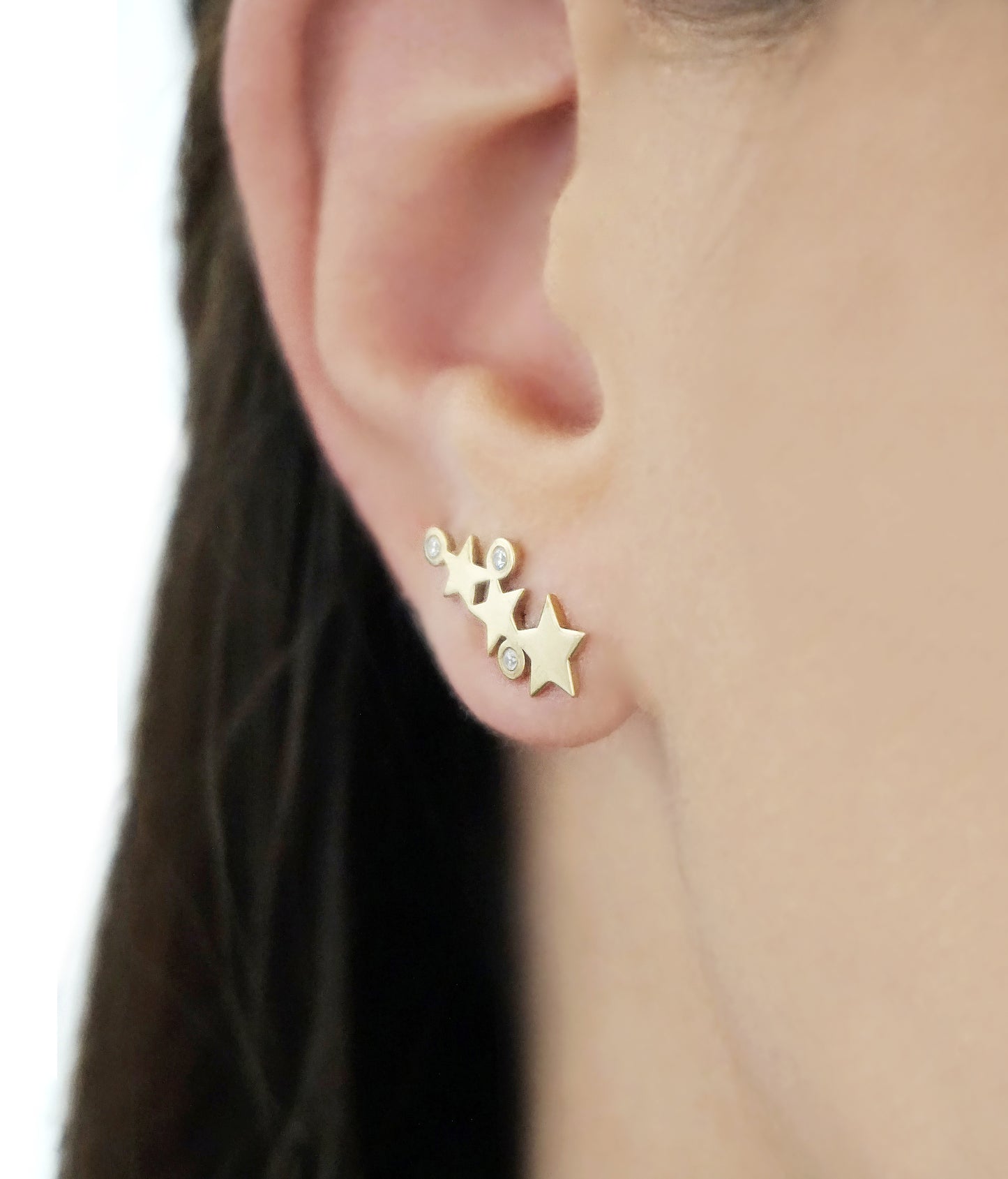 close up of a woman wearing 14K yellow gold triple star climber earrings with three tiny diamonds
