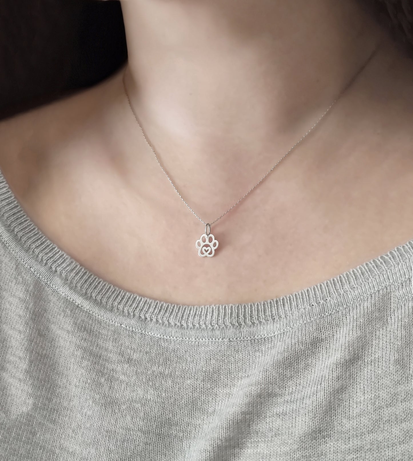 Woman wearing solid gold necklace with a tiny dog paw print pendant with a heart in the center