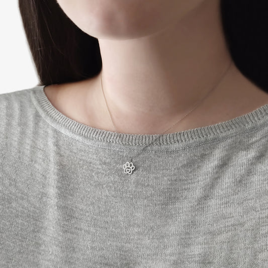 Female wearing solid gold necklace with a tiny dog paw print pendant with a heart in the center