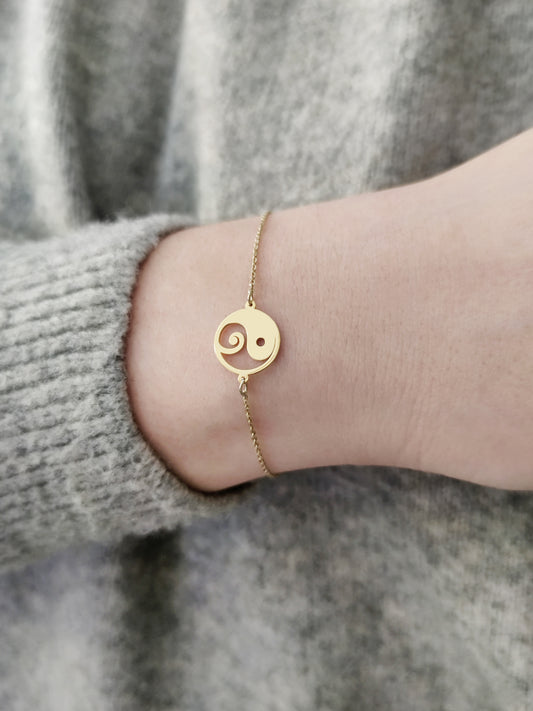 close up of a female wrist wearing a gold yin yang charm bracelet