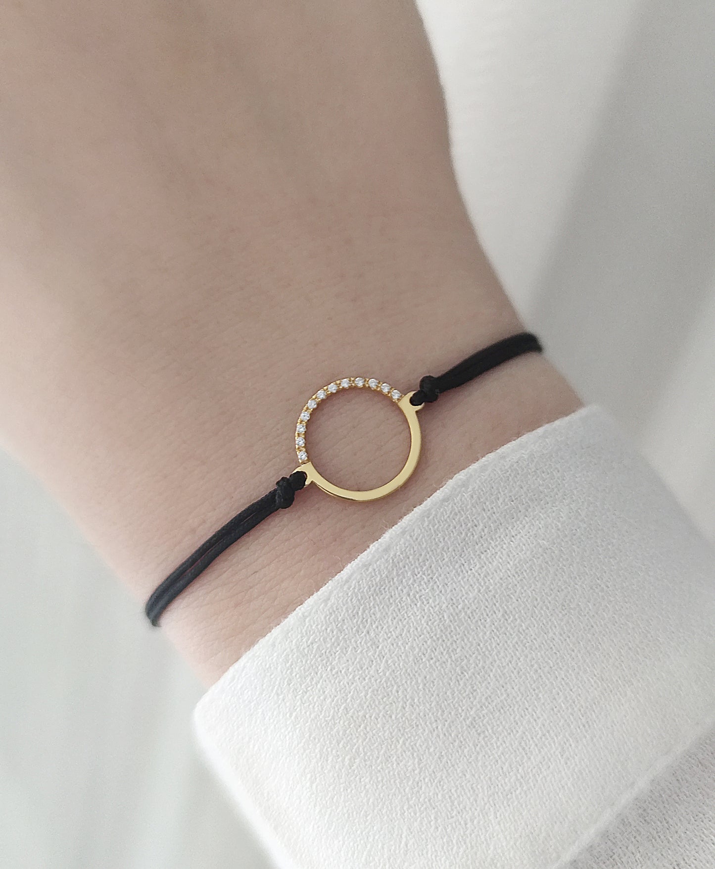 female wrist wearing solid yellow gold macrame bracelet with a circle charm set with 12 white diamonds on its two corners