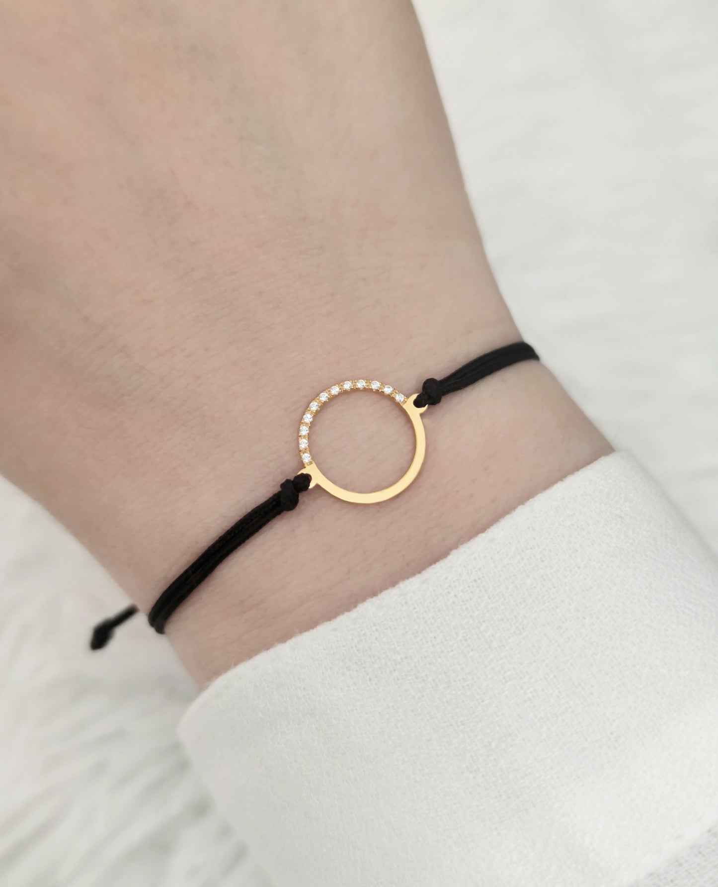 woman's wrist wearing solid yellow gold macrame bracelet with a circle charm set with 12 white diamonds on its two corners