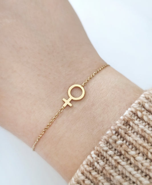 woman's wrist wearing a gold bracelet with a small venus female symbol charm