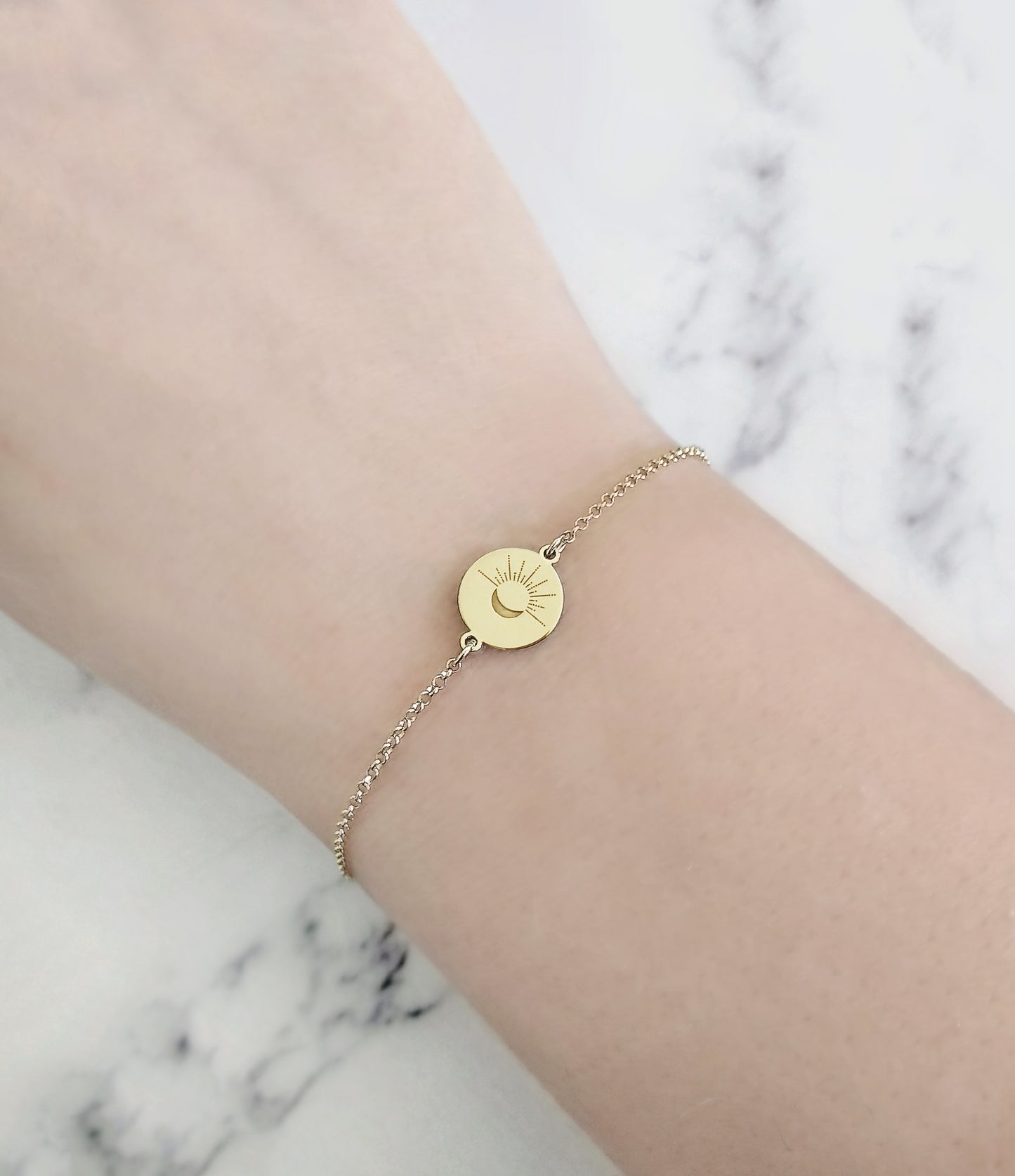 wmoan's wrist wearing yellow gold disc charm bracelet engraved with a crescent moon and sun rays