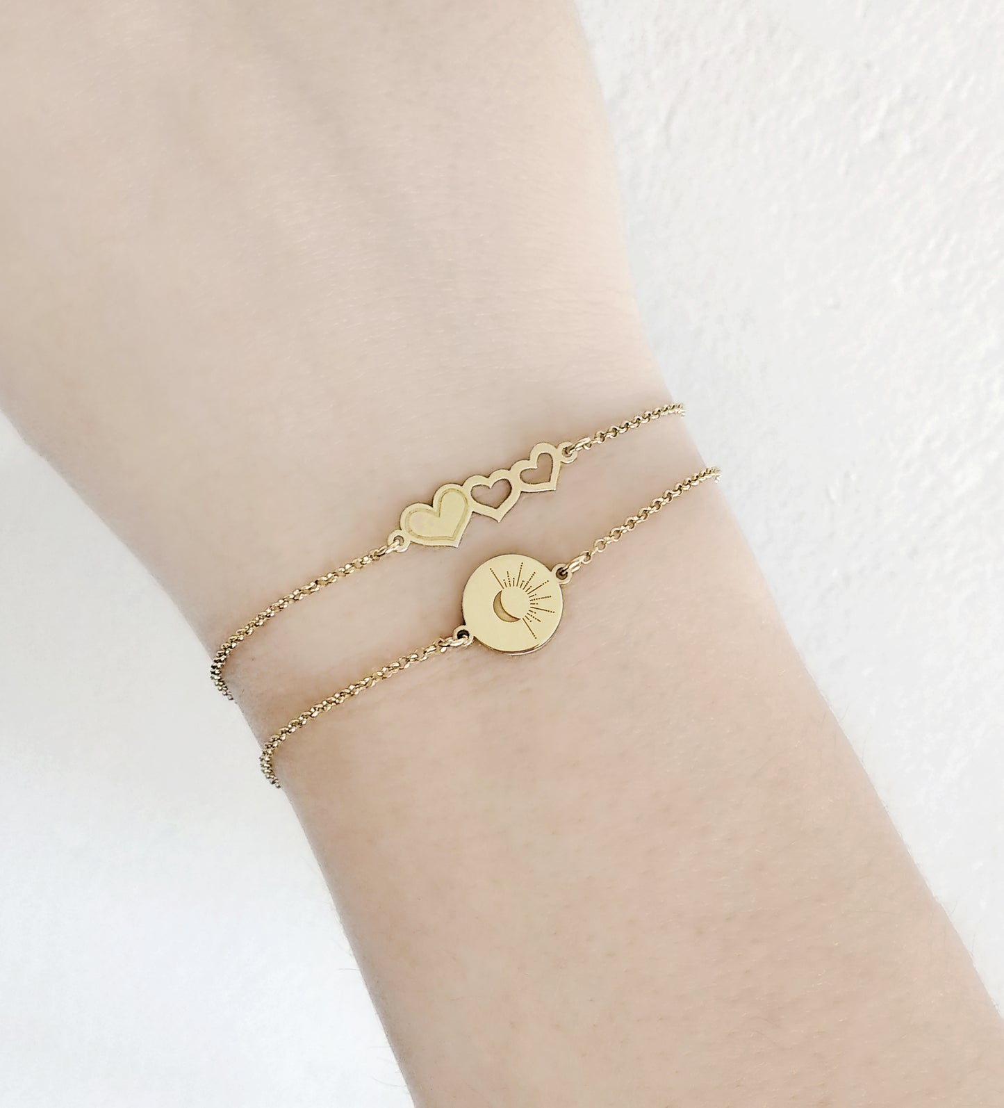 female wrist wearing yellow gold disc charm bracelet engraved with a crescent moon and sun rays and a triple hearts charm bracelet