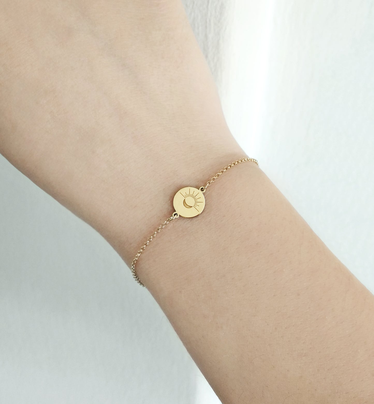 female wrist wearing yellow gold disc charm bracelet engraved with a crescent moon and sun rays