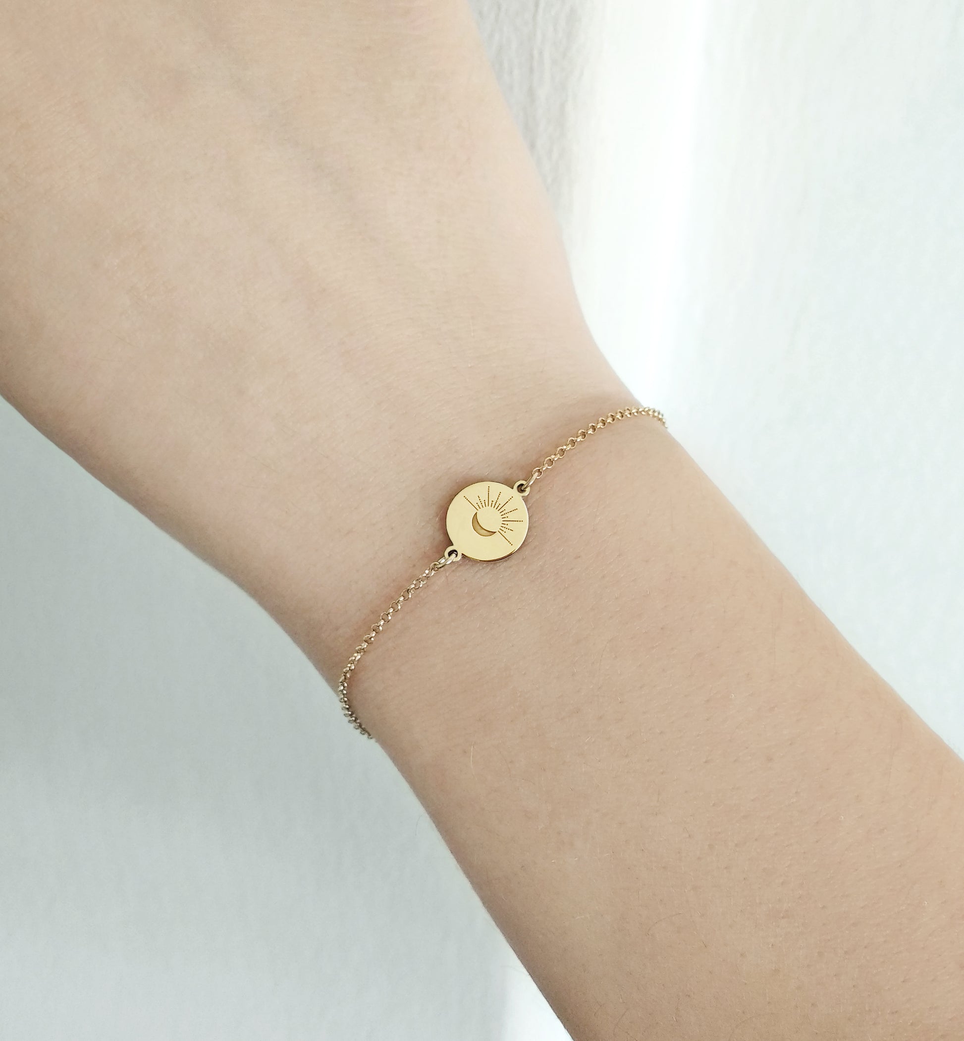 female wrist wearing yellow gold disc charm bracelet engraved with a crescent moon and sun rays