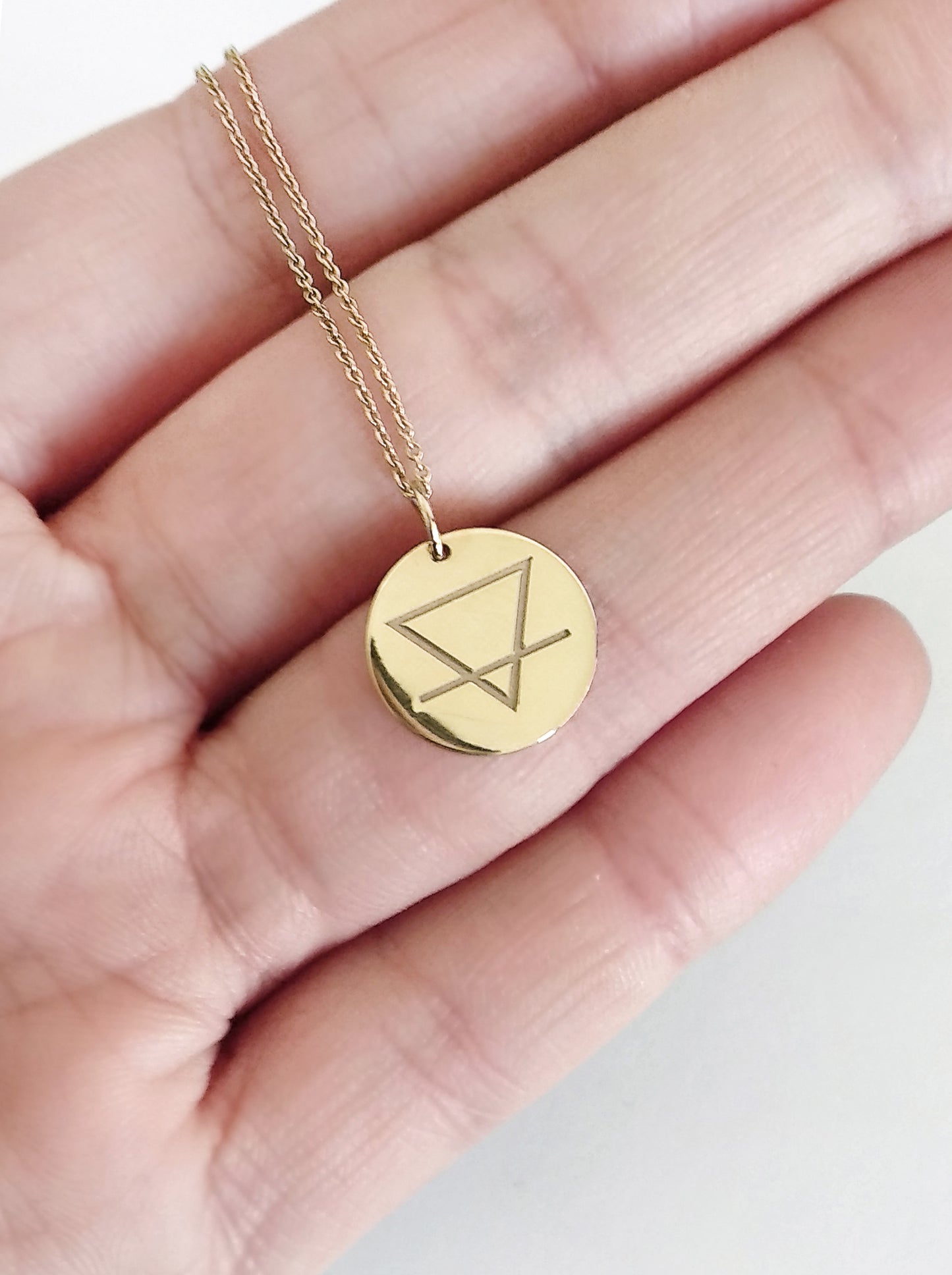 hand holding yellow gold necklace with a disc pendant engraved with the earth element for size reference