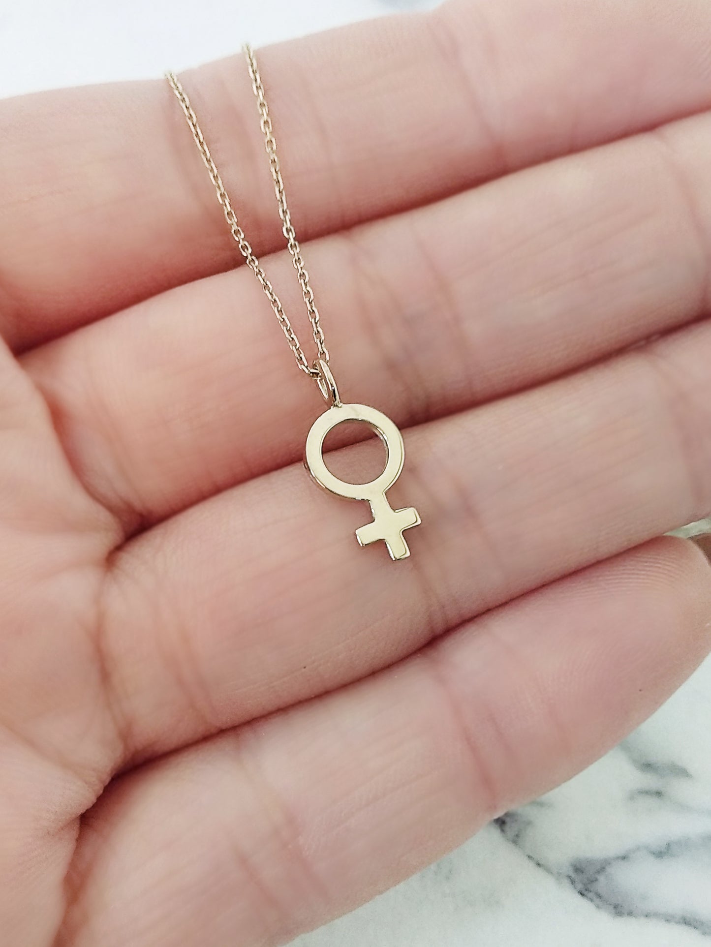 close up of a woman's palm holding a necklace with a small female symbol charm for size reference