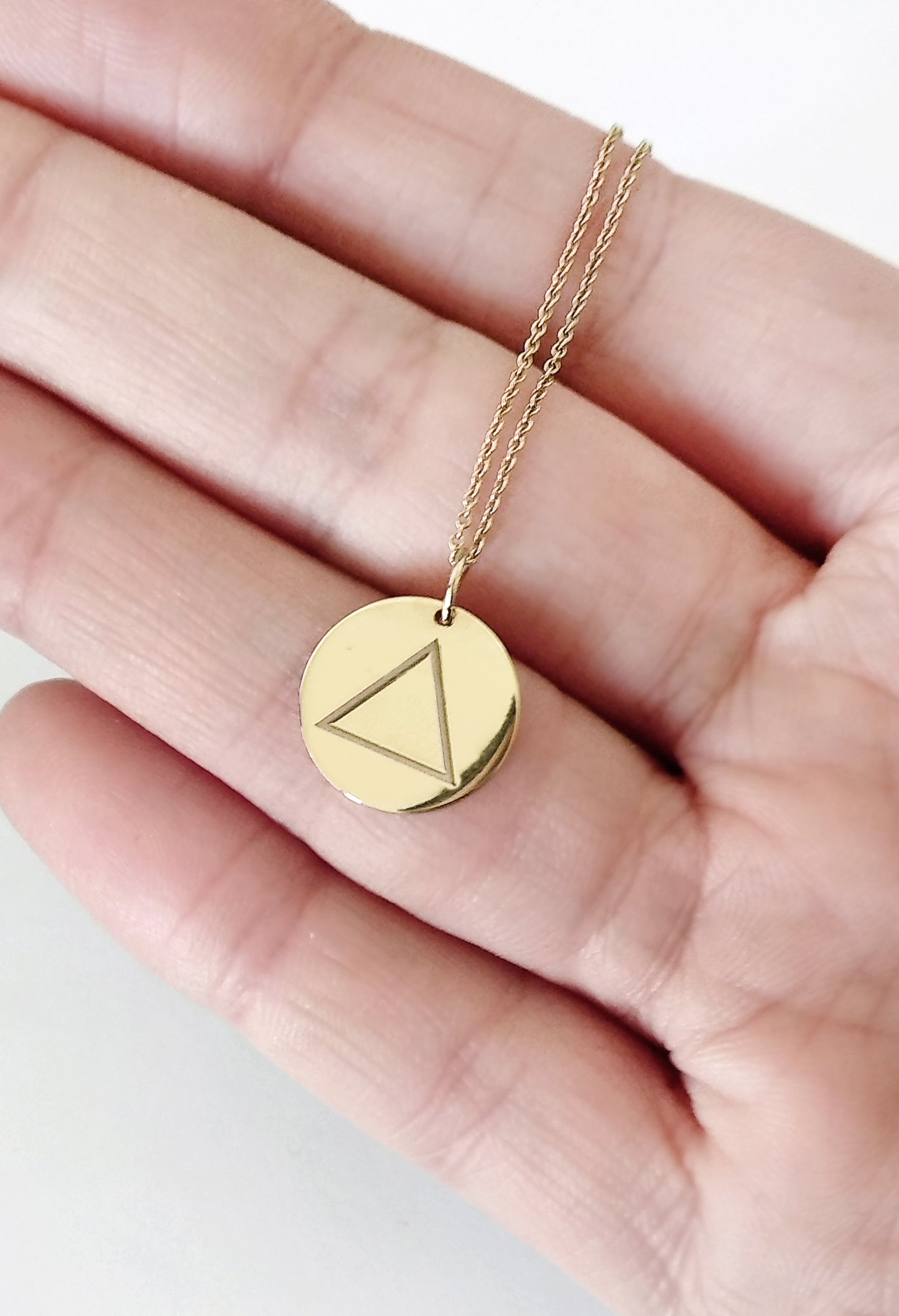 hand holding yellow gold necklace with a disc pendant engraved with the fire element for size reference