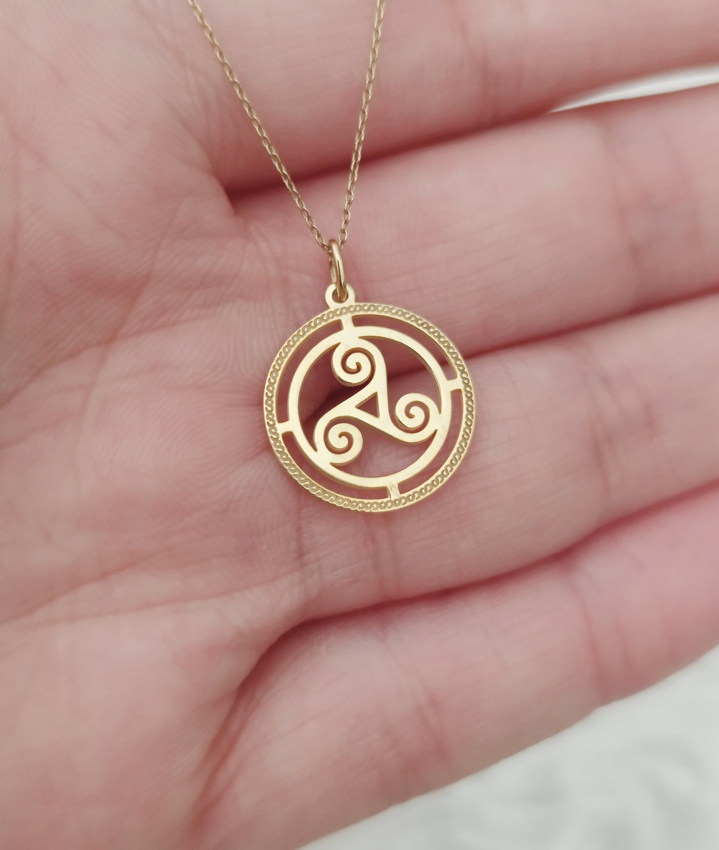 close up of a woman's palm holding a necklace with a circular triskelion knot pendant with cutouts and an engraved frame