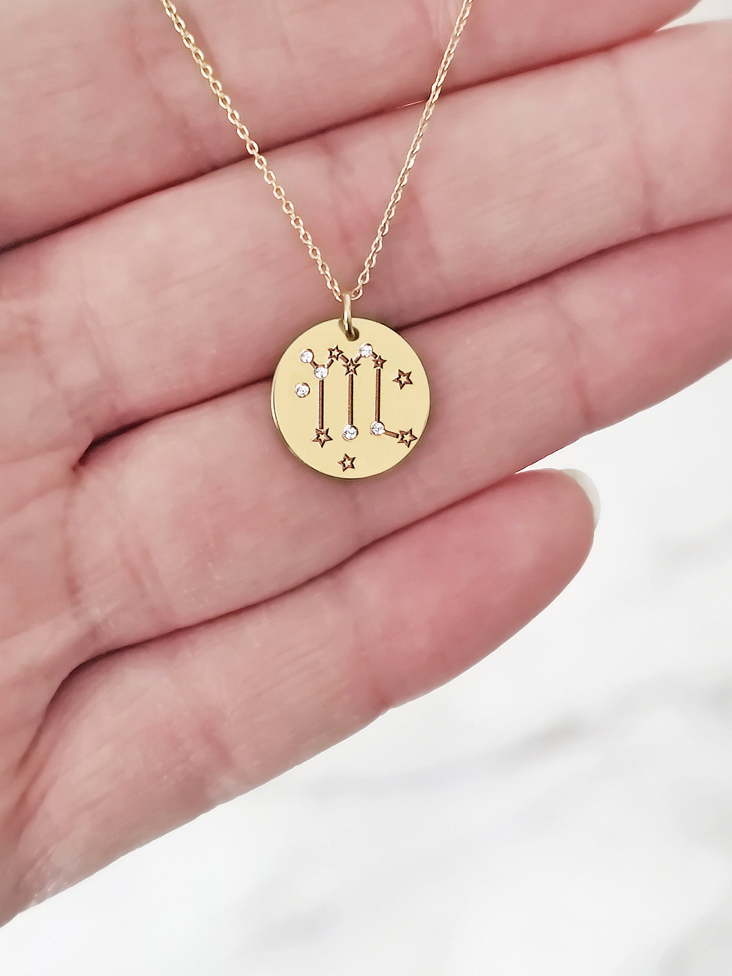 hand holding a gold necklace with a 14mm disc pendant engraved with the scorpio zodiac sign and set with six tiny diamonds