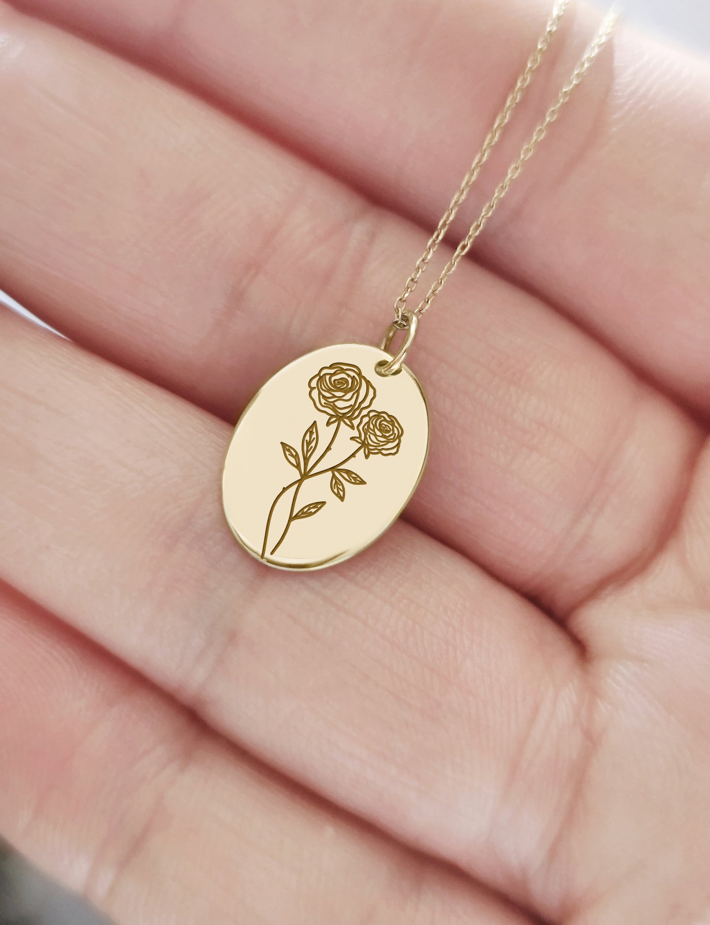 hand holding a solid yellow gold oval pendant necklace engraved with a Rose the birth flower of June