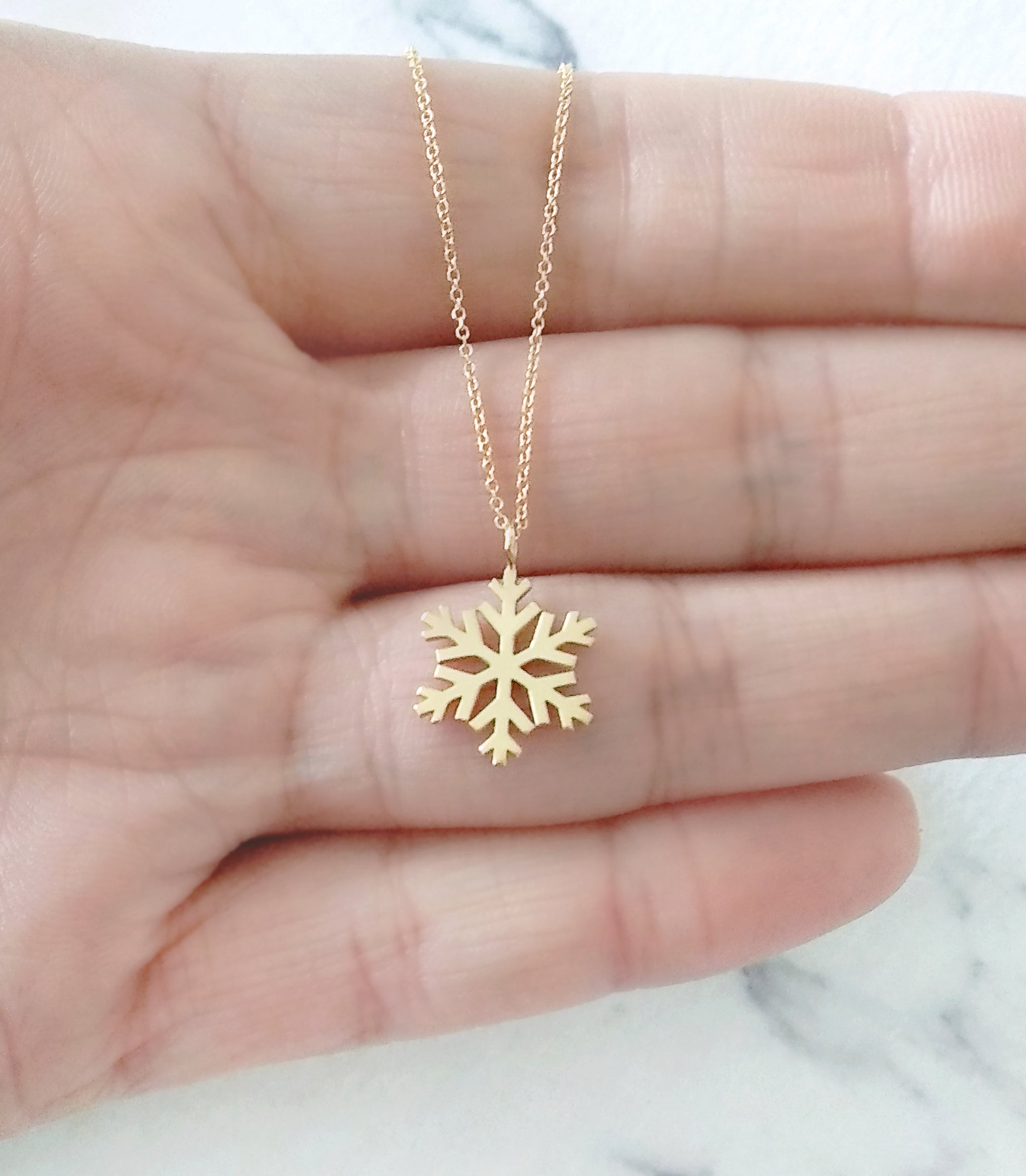 close up of a palm holding a gold necklace with a small pendant in the shape of a snowflake for size reference