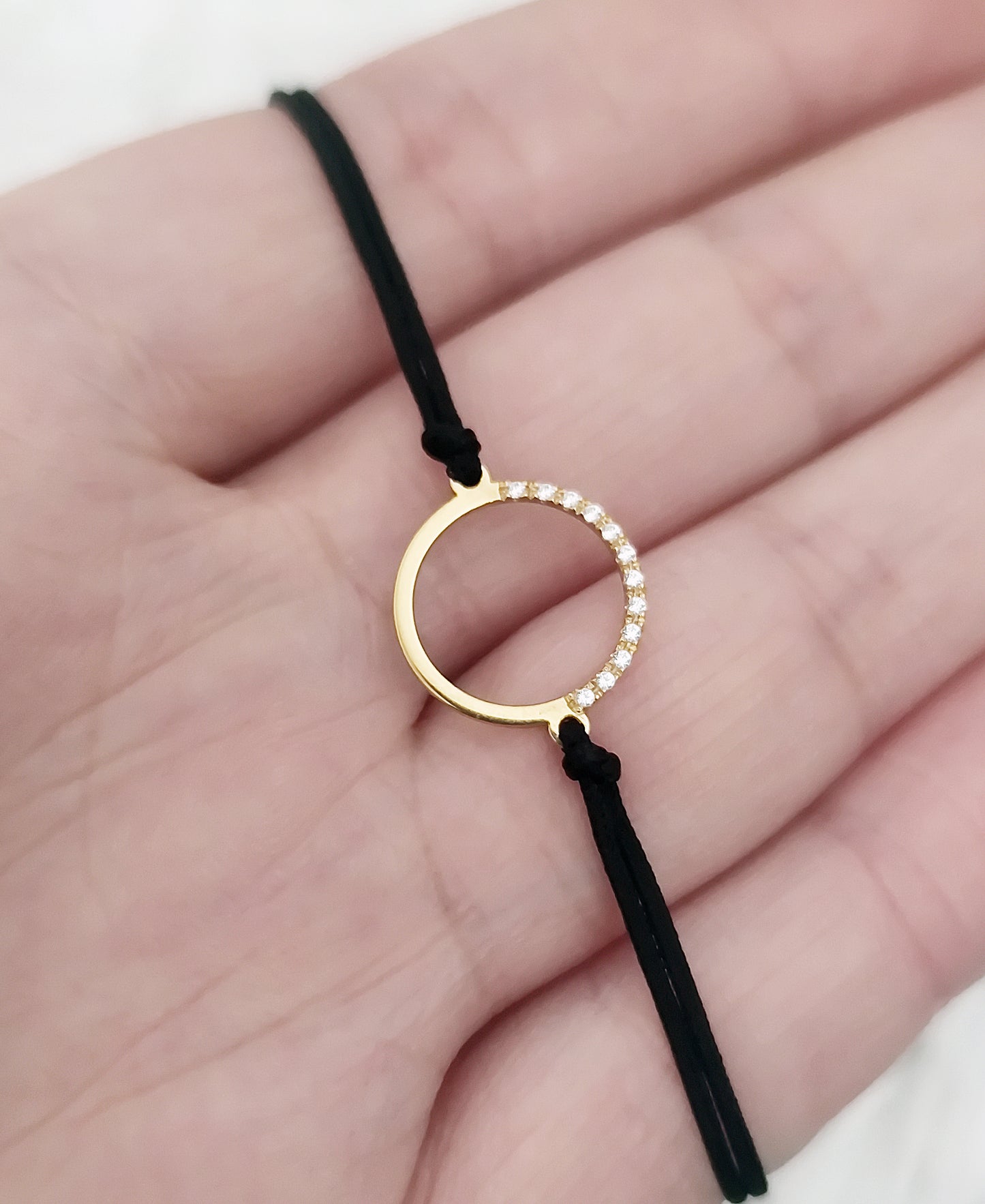 hand holding a solid yellow gold macrame bracelet with a circle charm set with 12 white diamonds on its two corners