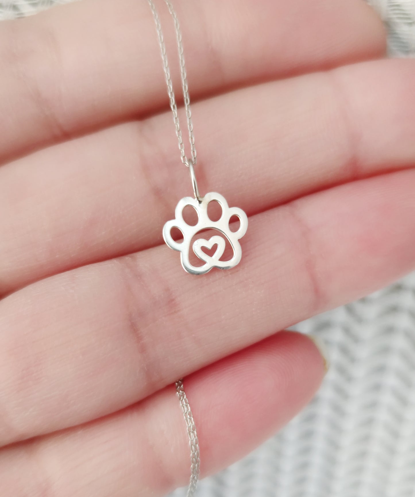 hand holding solid gold necklace with a tiny dog paw print pendant with a heart in the center