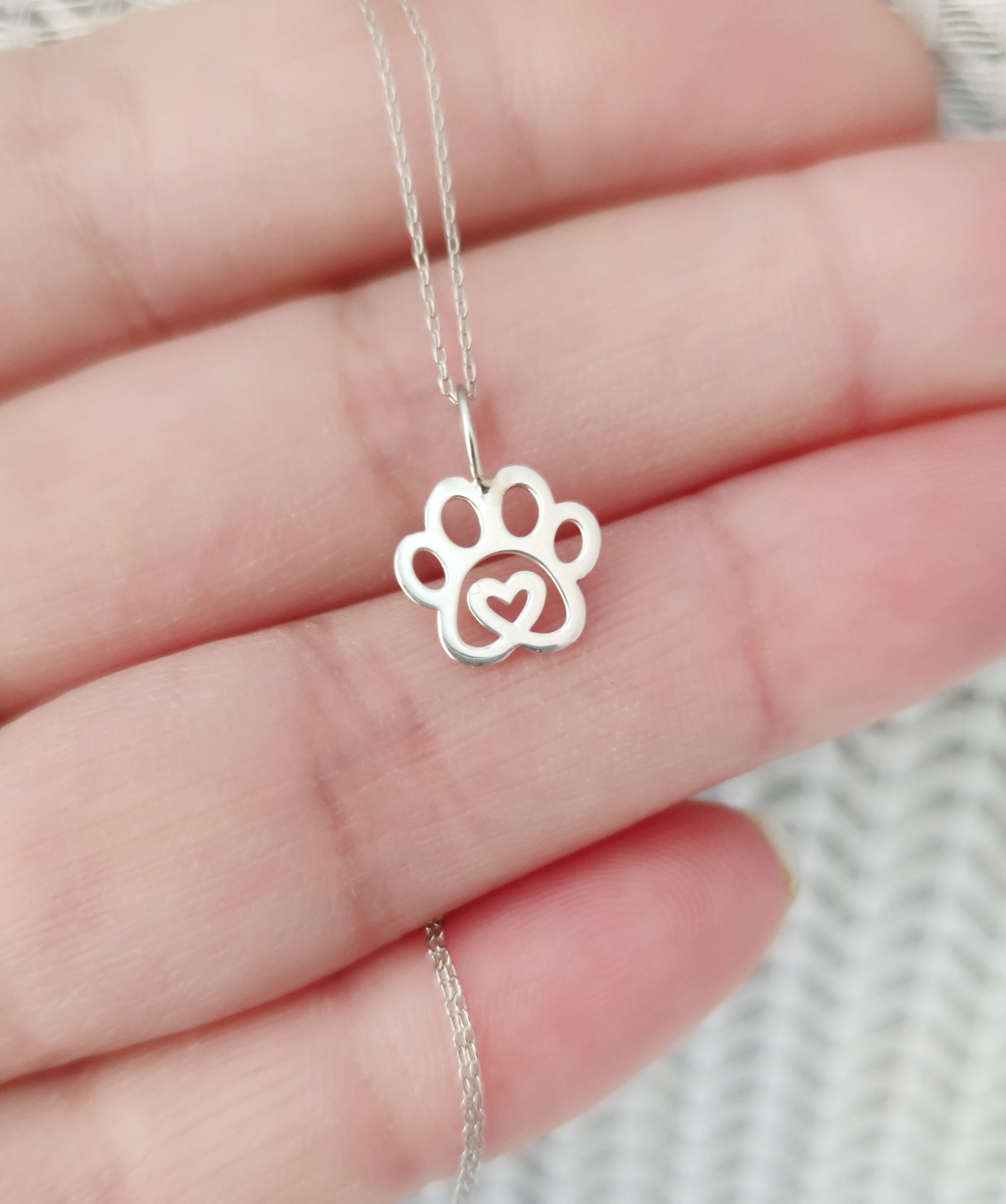 hand holding solid gold necklace with a tiny dog paw print pendant with a heart in the center