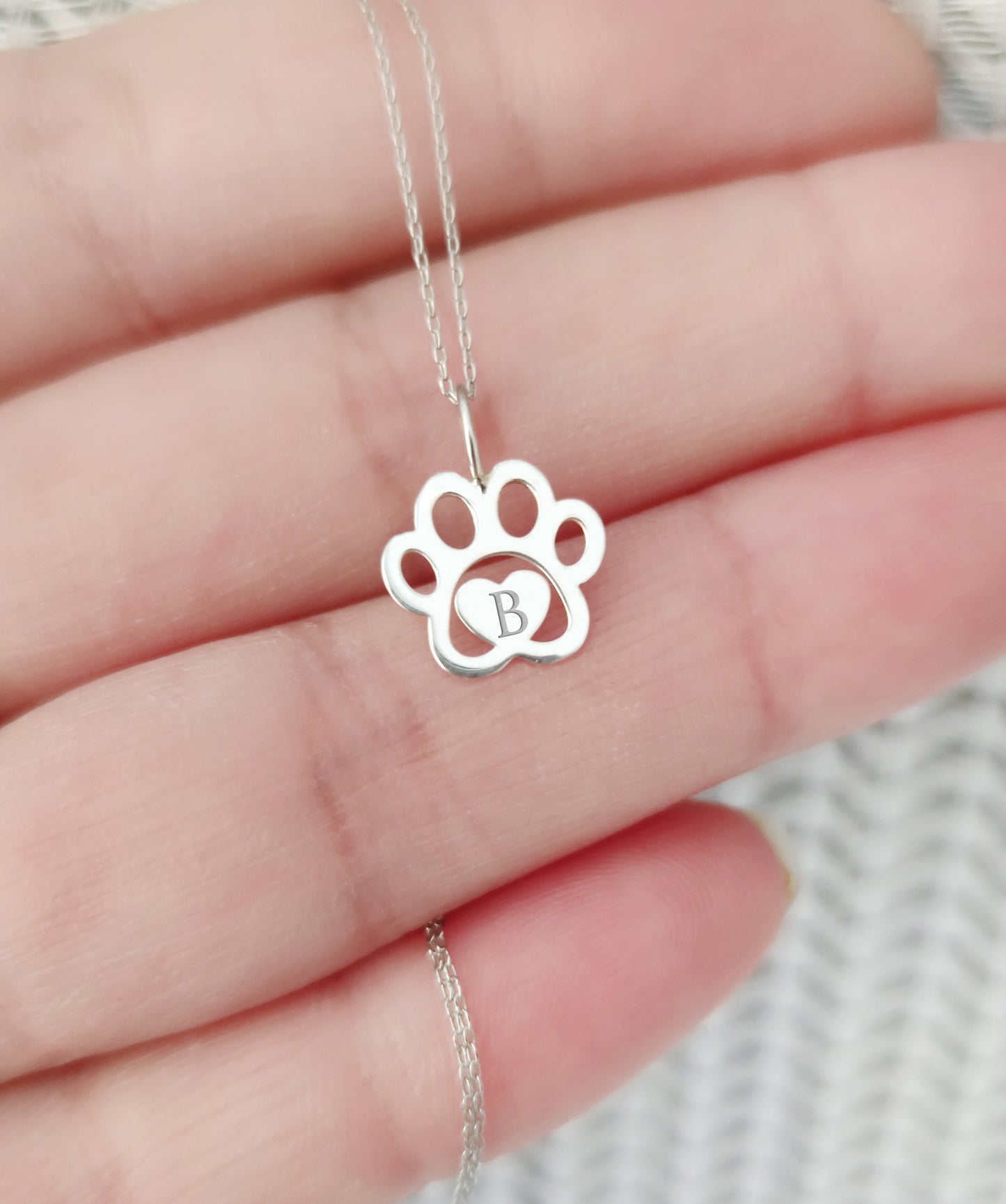 hand holding a white gold necklace with a dog paw print pendant engraved with a monogram