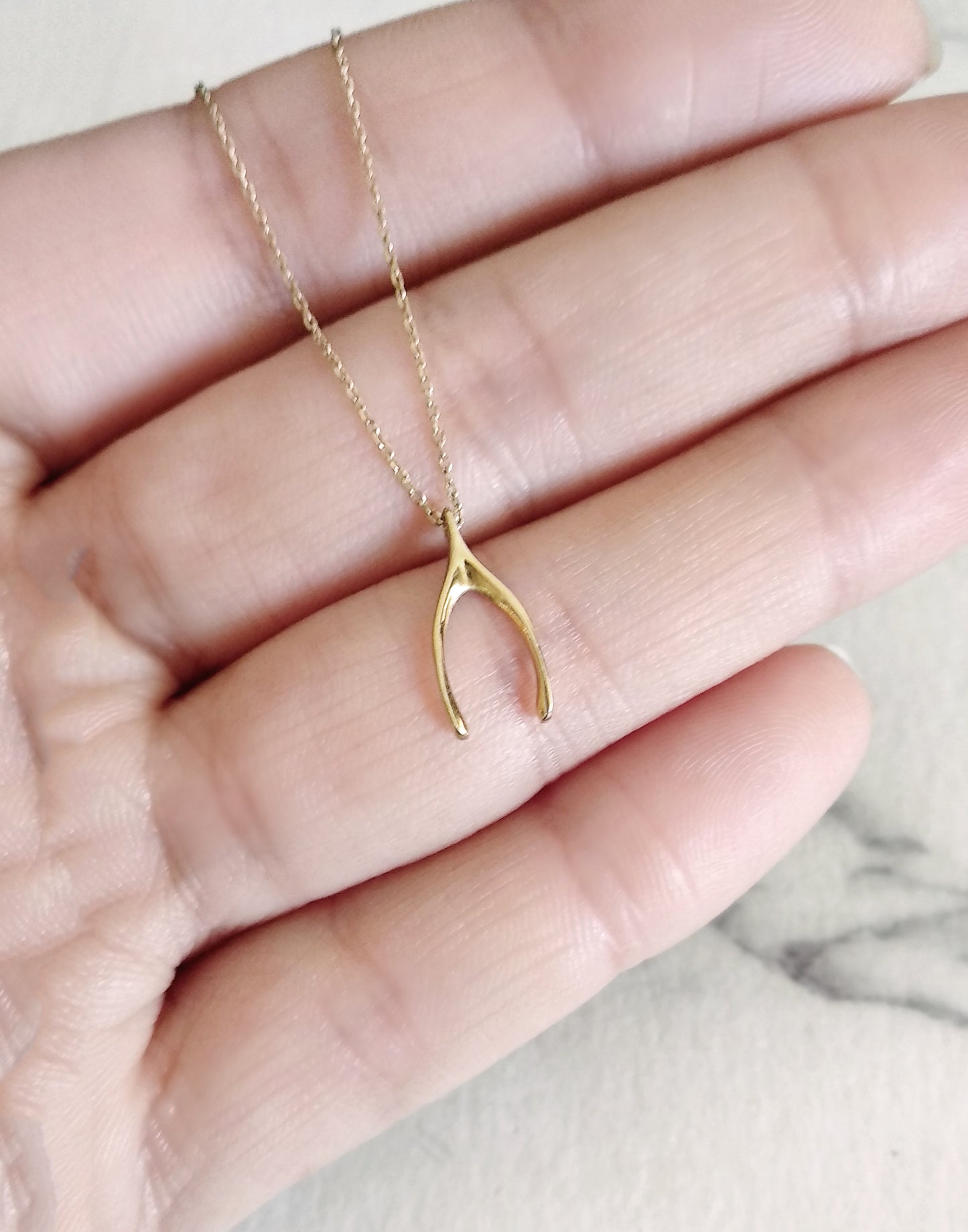 hand holding a yellow gold necklace with a tiny wishbone charm for size reference