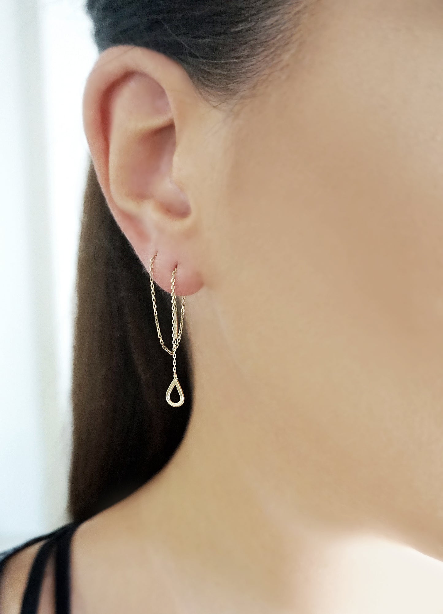 woman wearing yellow gold threader earring with a tiny teardrop pulled through two piercings