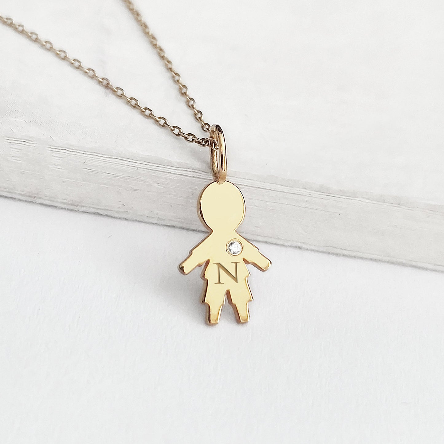 close up of a yellow gold necklace with tiny boy outline charm engraved with a monogram and set with tiny diamond