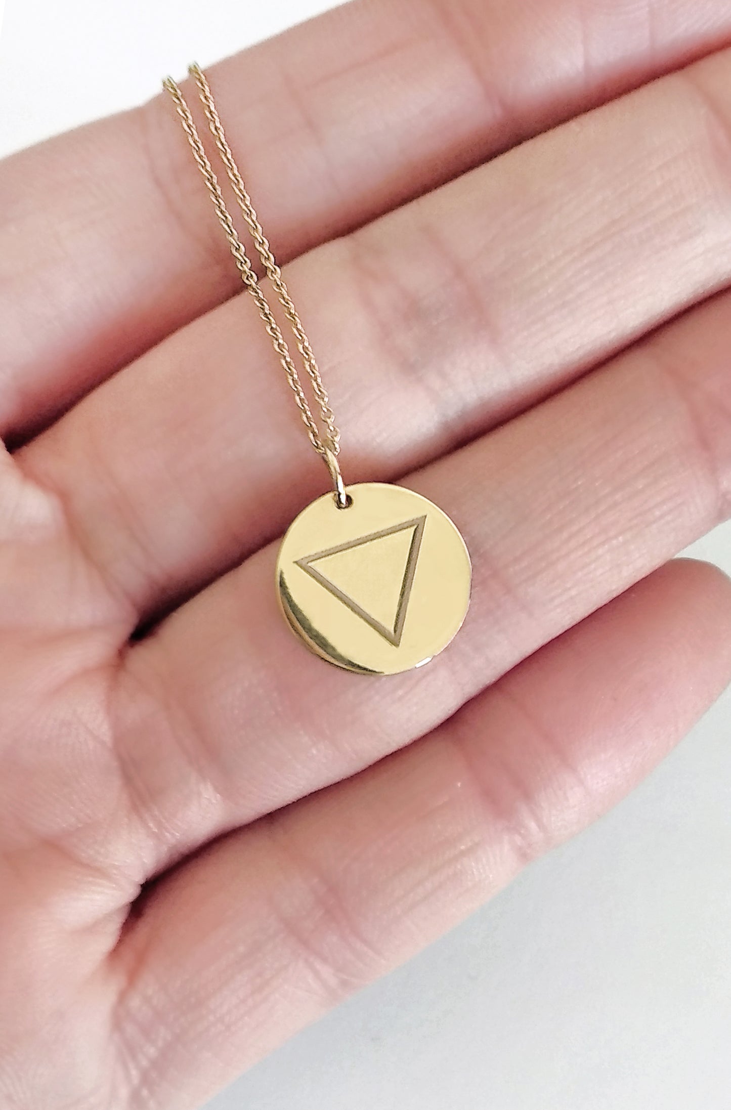 hand holding yellow gold necklace with a disc pendant engraved with the water element for size reference