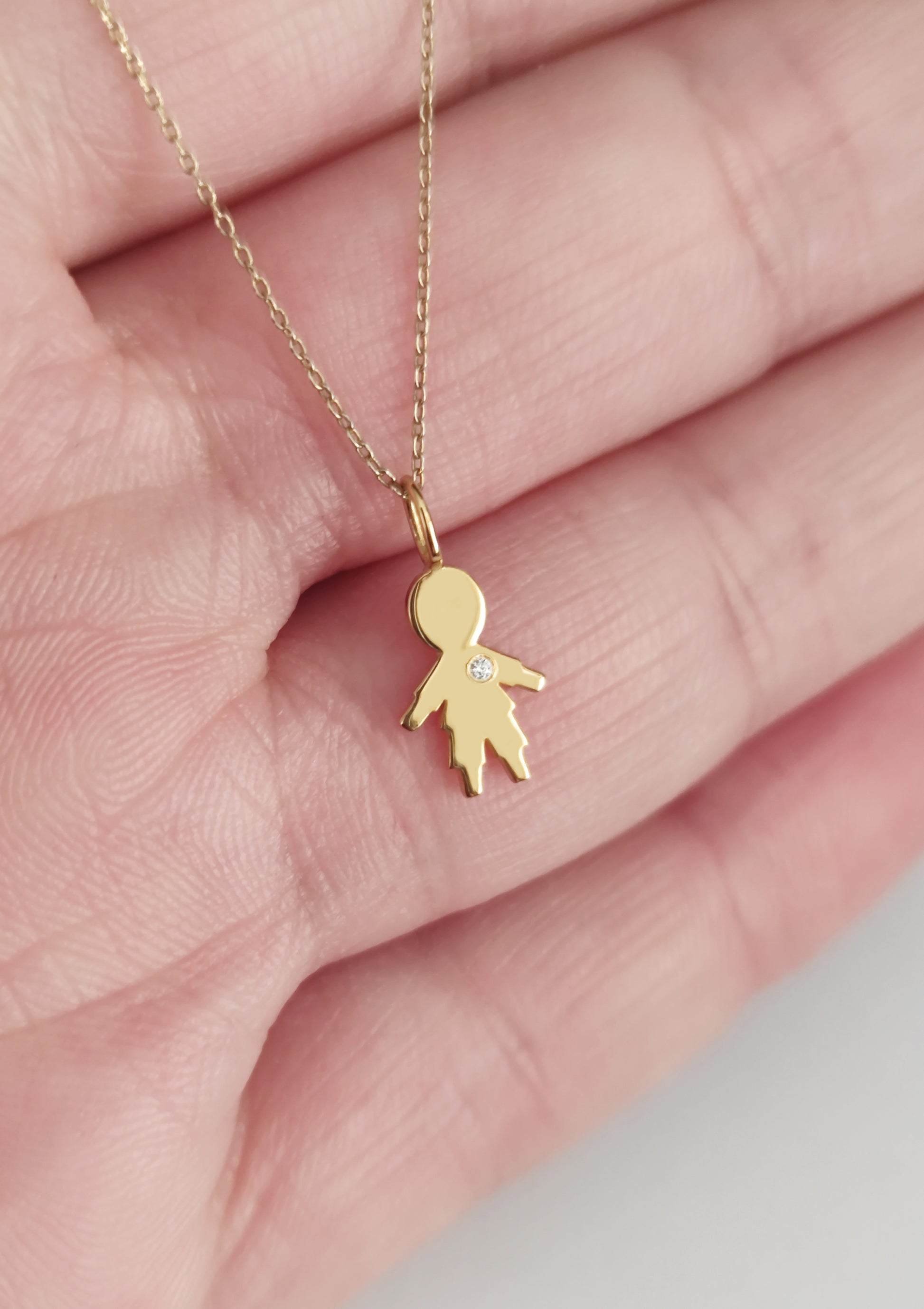close up of a palm holding a gold necklace with a tiny boy outline charm set with a diamond