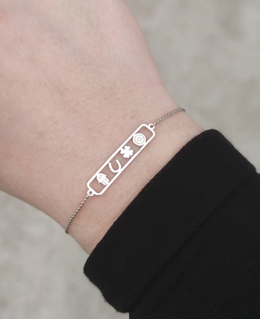 female wrist wearing an open bar bracelet with four lucky charms, a hamsa, a horseshoe, a clover and an evil eye made in solid gold