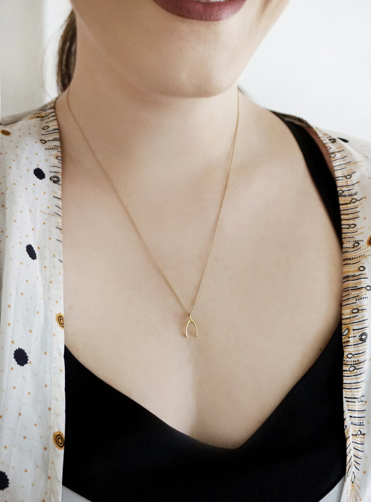 female wearing a long necklace with a tiny wishbone charm in solid yellow gold