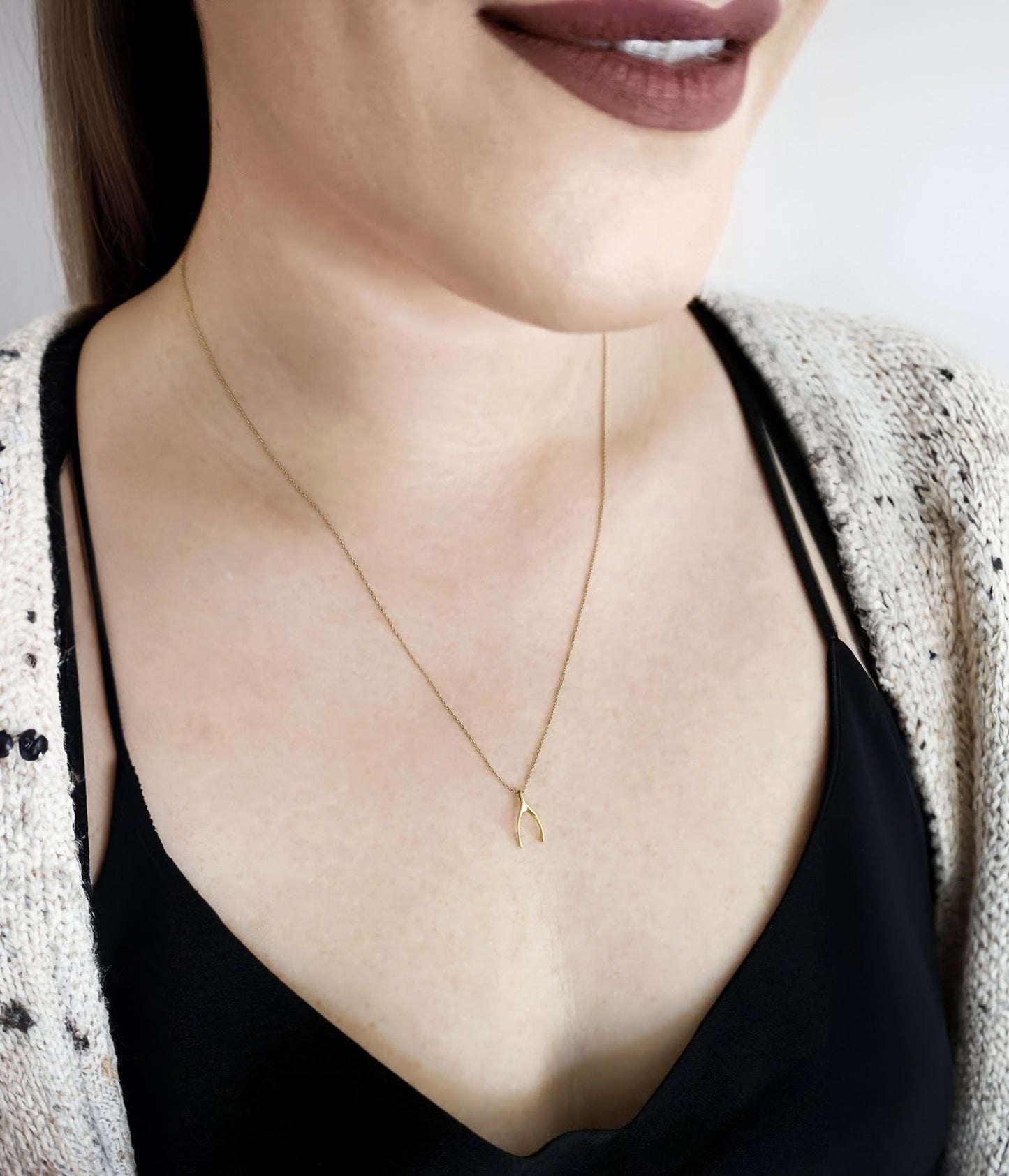 woman wearing a dainty solid gold necklace with a tiny wishbone charm