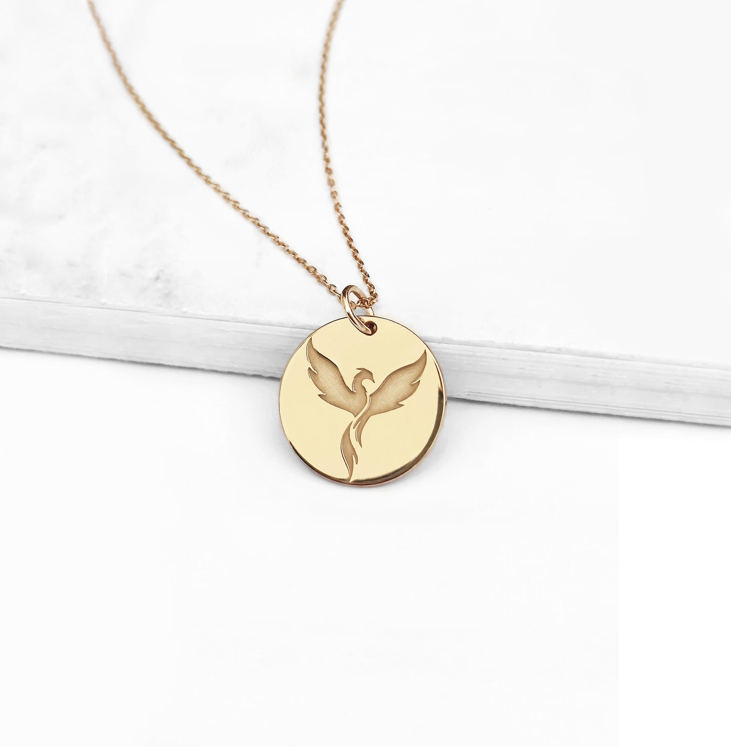 close up of a yellow gold pendant necklace engraved with a phoenix firebird