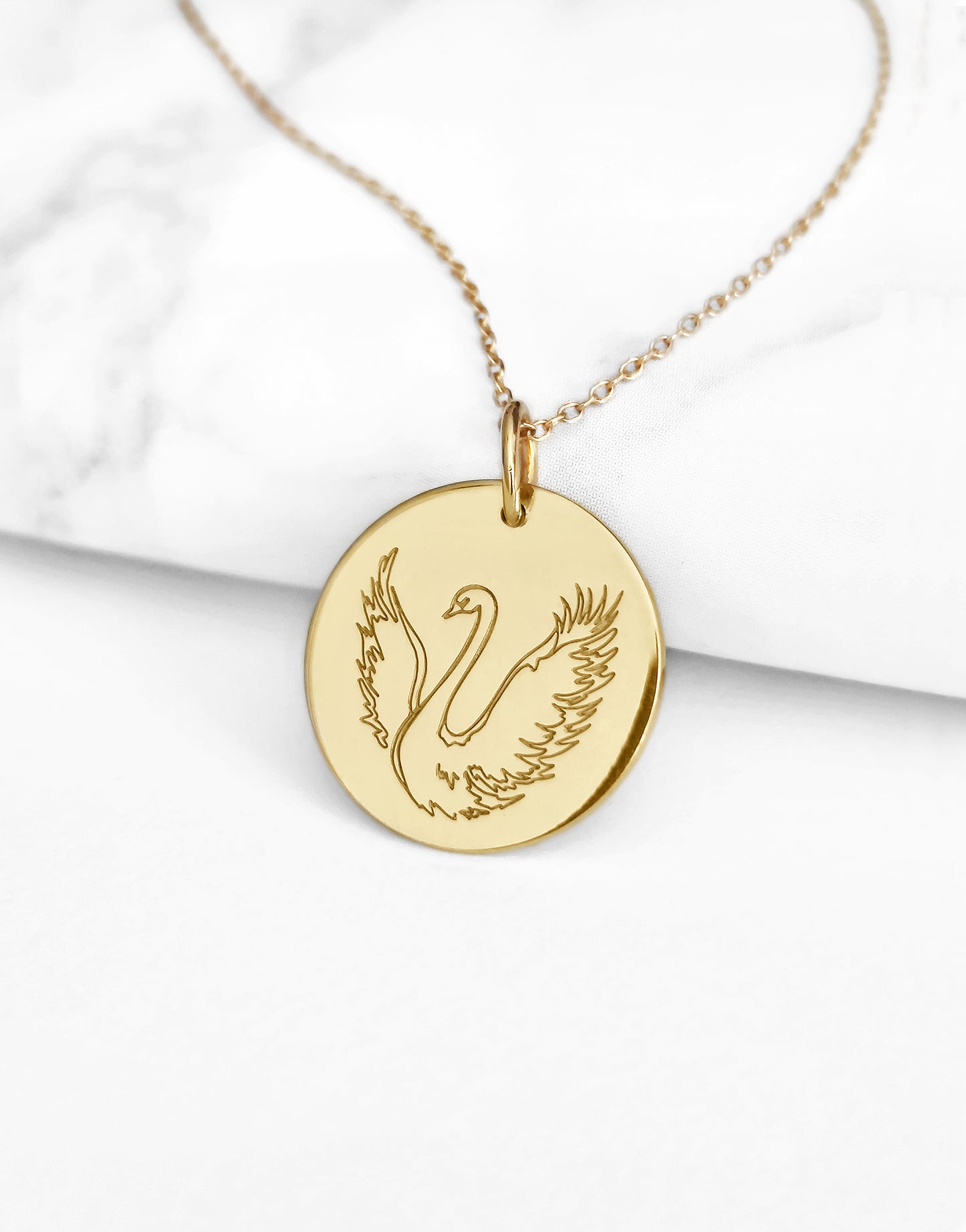 close up of yellow gold necklace with a 14mm disc pendant engraved with a swan with open wings