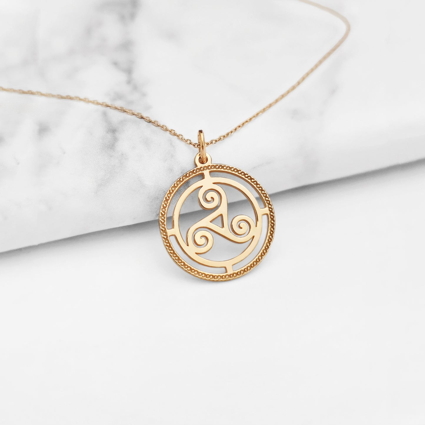 close up of a solid yellow gold necklace with a cutout triskelion celtic knot pendant and an engraved frame