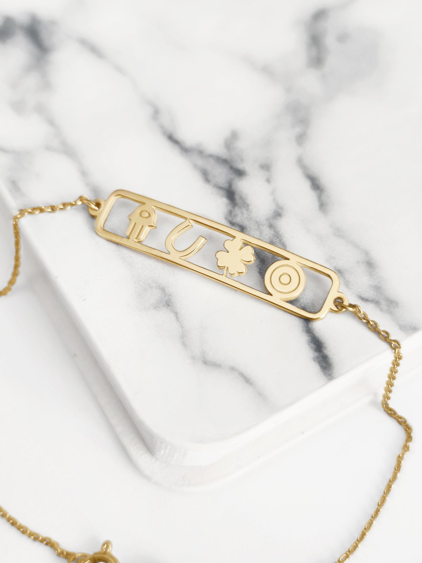 14K gold open bar bracelet with four lucky charms, a hamsa, a horseshoe, a clover and an evil eye