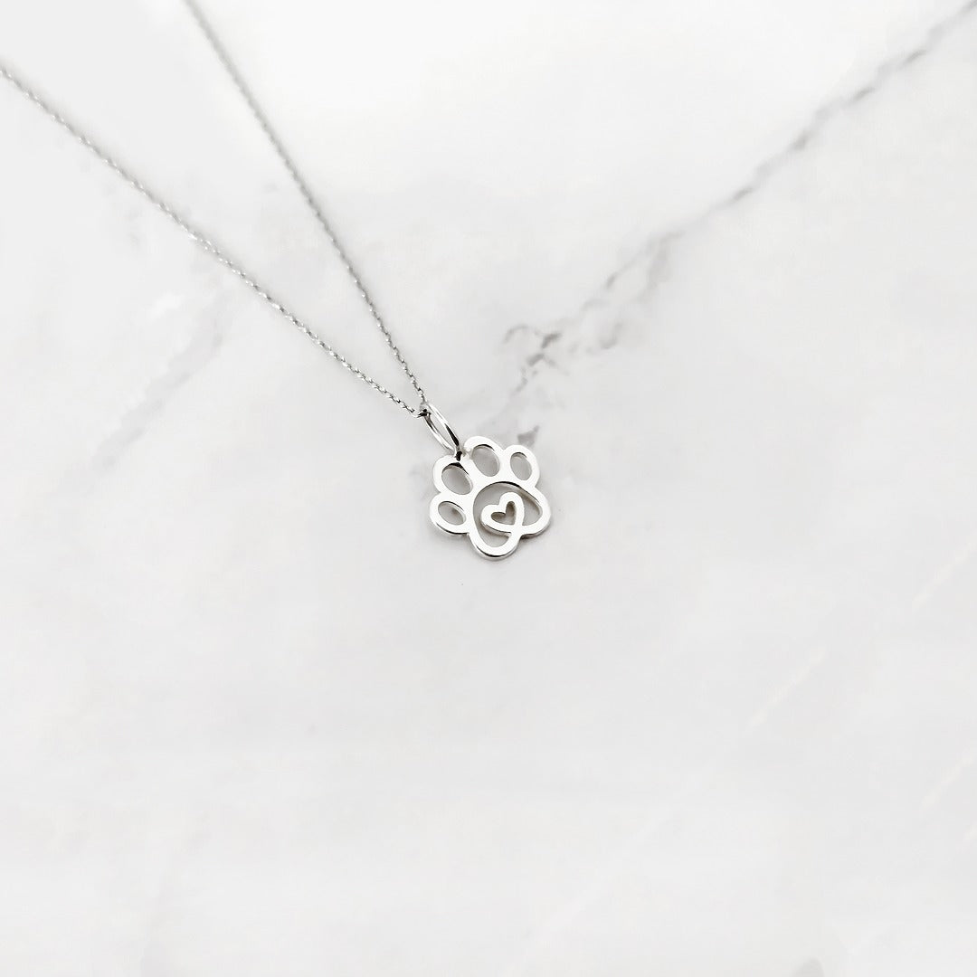 White gold paw print necklace with a heart in the middle on a white marble background
