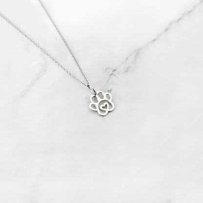 White gold paw print necklace with a heart in the middle on a white marble background