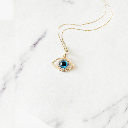Yellow gold necklace with an eye-shaped pendant featuring a blue eye in the center surrounded by white diamonds on a marble surface