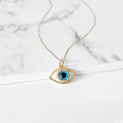 Gold necklace with an eye-shaped pendant featuring a blue eye in the center surrounded by white diamonds on a marble surface